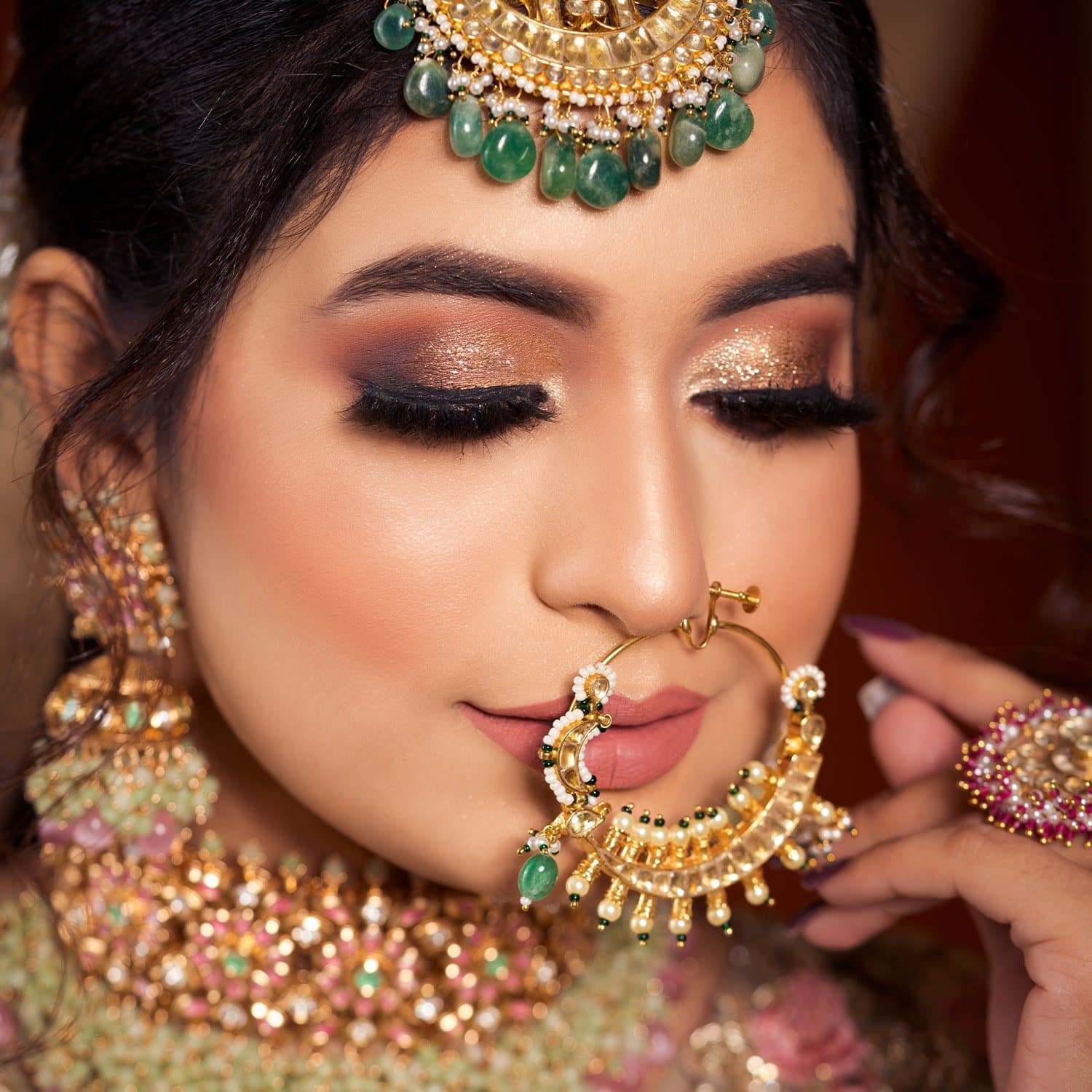 Close-up of glittering gold bridal eye makeup with a pearl nath and emerald jewellery
