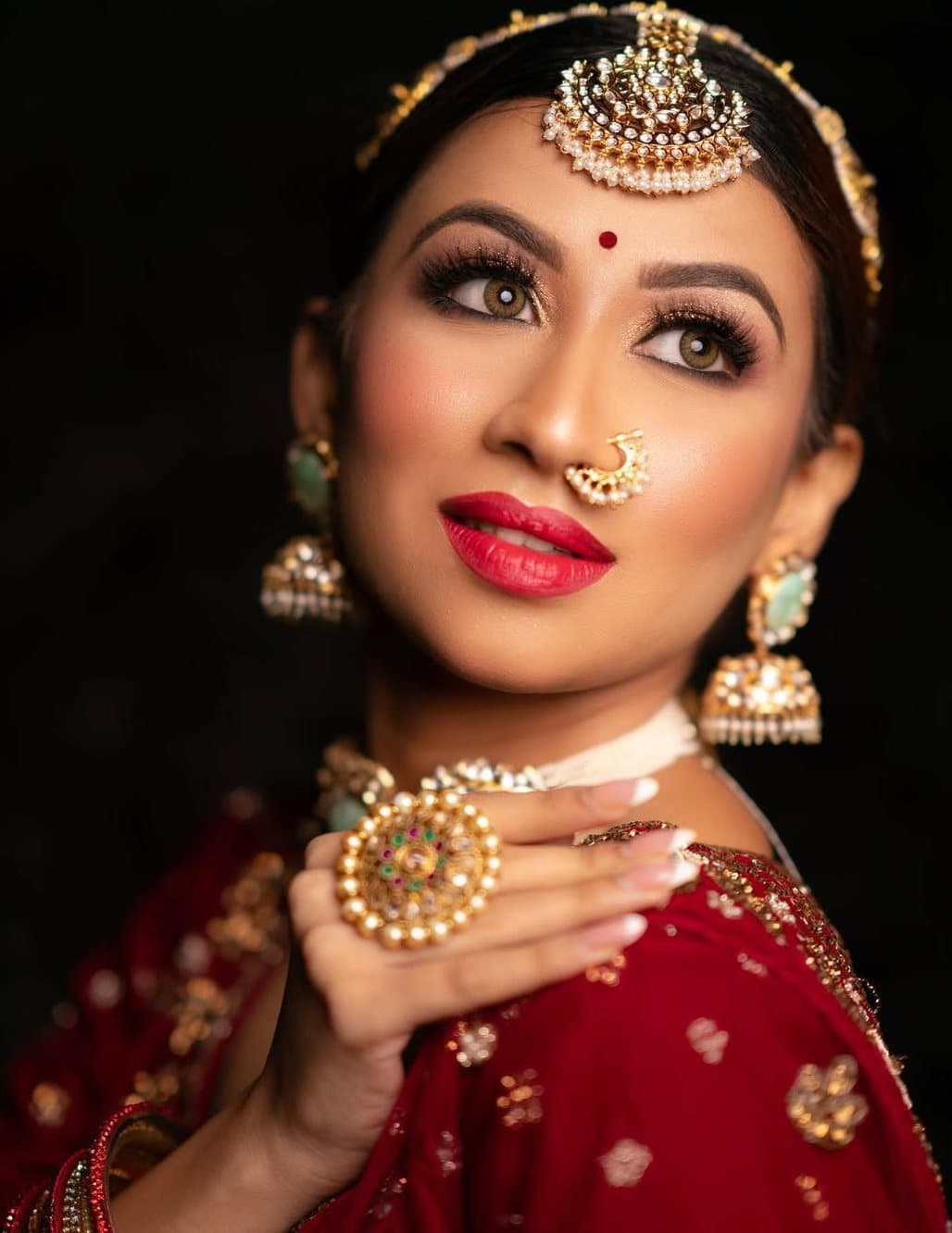 Bride in red with a gold maang tikka, jhumkas and a bold red lip